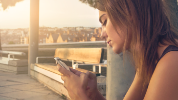 Une femme assise sur un banc regarde son téléphone.