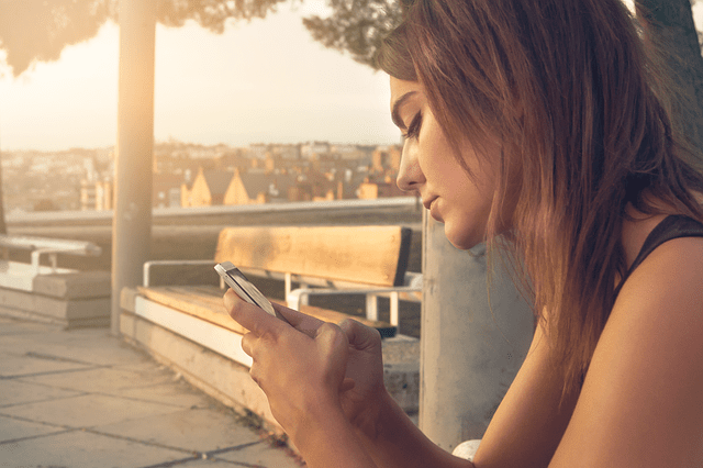 Une femme assise sur un banc regarde son téléphone.