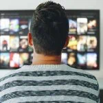 Un homme assis devant une télévision regarde des films.