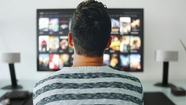 Un homme assis devant une télévision regarde des films.