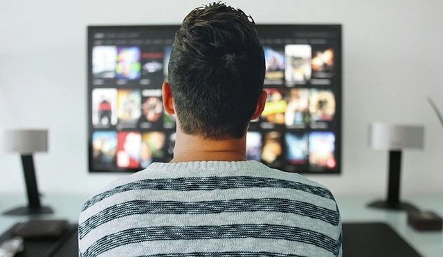 Un homme assis devant une télévision regarde des films.