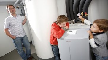 Un homme et deux enfants devant un chauffe-eau.