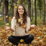 Une jeune femme assise par terre, les mains tendues, découvrant des techniques pour renforcer sa confiance en elle pour un quotidien plus heureux.