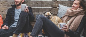 Deux personnes assises sur un banc en bois avec un chien et une tasse de café.