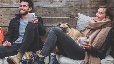 Deux personnes assises sur un banc en bois avec un chien et une tasse de café.