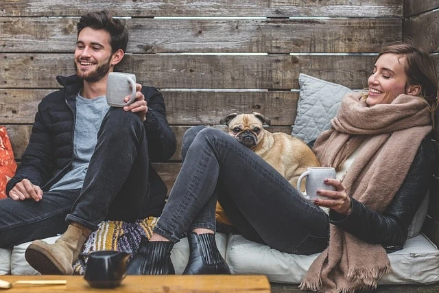 Deux personnes assises sur un banc en bois avec un chien et une tasse de café.