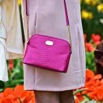 Une femme tenant un sac à main rose devant des tulipes.