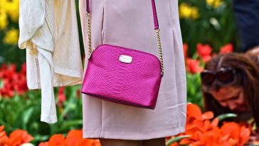 Une femme tenant un sac à main rose devant des tulipes.