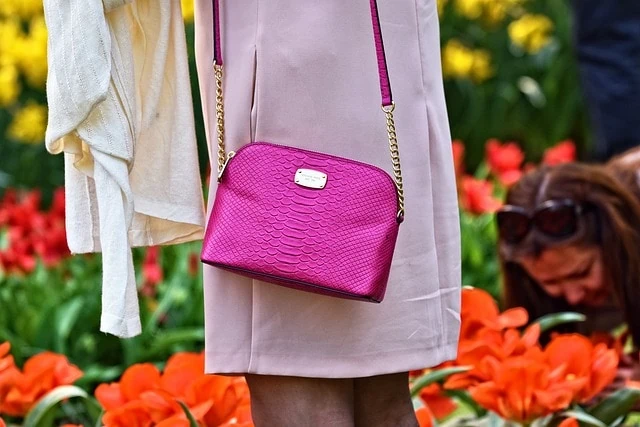 Une femme tenant un sac à main rose devant des tulipes.