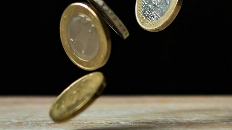 Deux pièces en euros tombant sur une table en bois, symbolisant l'aspect philanthropique de la démocratie.