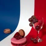 Une table rouge, blanche et bleue agrémentée d'un verre de vin et d'un macaron, évoquant l'ambiance d'un voyage typiquement français.