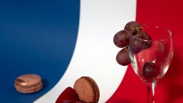 Une table rouge, blanche et bleue agrémentée d'un verre de vin et d'un macaron, évoquant l'ambiance d'un voyage typiquement français.