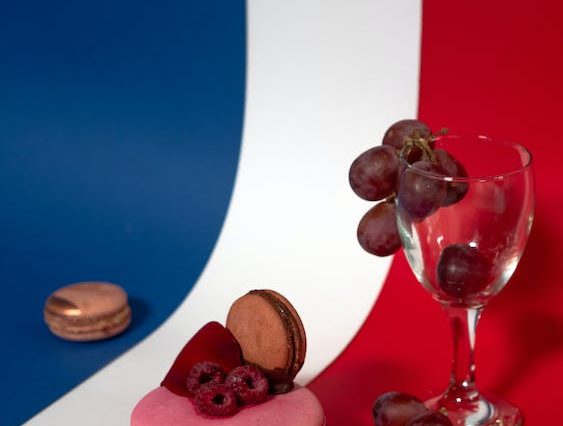 Une table rouge, blanche et bleue agrémentée d'un verre de vin et d'un macaron, évoquant l'ambiance d'un voyage typiquement français.