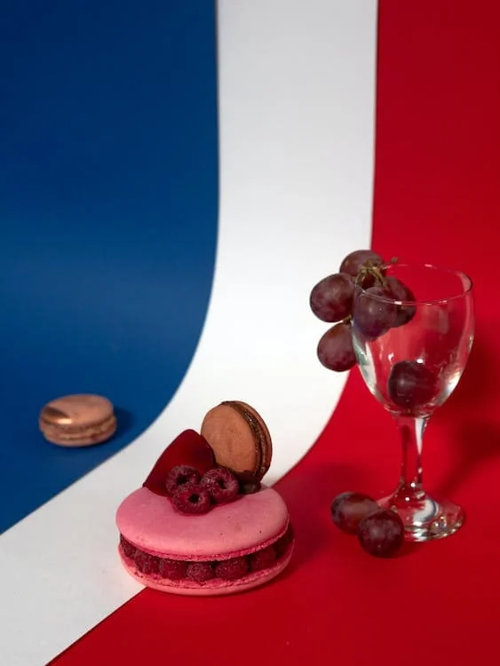 Une table rouge, blanche et bleue agrémentée d'un verre de vin et d'un macaron, évoquant l'ambiance d'un voyage typiquement français.