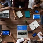 Un groupe de personnes assises autour d’une table utilisant des ordinateurs portables pour la communication publique.