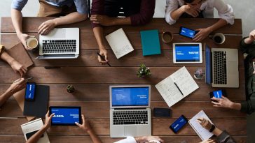 Un groupe de personnes assises autour d’une table utilisant des ordinateurs portables pour la communication publique.