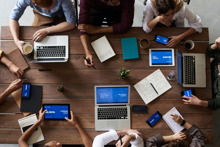 Un groupe de personnes assises autour d’une table utilisant des ordinateurs portables pour la communication publique.