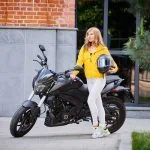 Une femme en veste jaune debout à côté d’une moto.