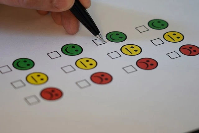 Main tenant un stylo pour cocher une case sur un papier d'enquête avec des icônes colorées de smiley et de visage triste indiquant différents niveaux de satisfaction au travail.
