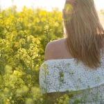 Une femme se tient debout dans un champ de fleurs jaunes et montre comment s'épanouir.