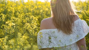 Une femme se tient debout dans un champ de fleurs jaunes et montre comment s'épanouir.