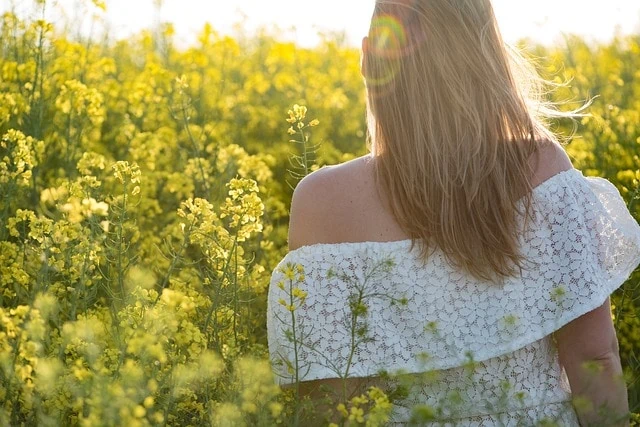 Une femme se tient debout dans un champ de fleurs jaunes et montre comment s'épanouir.