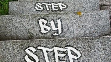 Escalier en béton avec "étapes clés" peintes sur les marches, entouré de verdure.