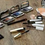 Produits de maquillage assortis, notamment des palettes de fards à paupières, du mascara et des pinceaux pour réaliser du maquillage, dispersés sur une surface en bois.