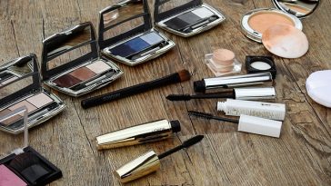 Produits de maquillage assortis, notamment des palettes de fards à paupières, du mascara et des pinceaux pour réaliser du maquillage, dispersés sur une surface en bois.