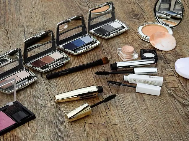 Produits de maquillage assortis, notamment des palettes de fards à paupières, du mascara et des pinceaux pour réaliser du maquillage, dispersés sur une surface en bois.