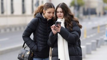 Deux jeunes femmes en vestes d'hiver regardant ensemble un iPhone haut de gamme dans une rue de la ville.