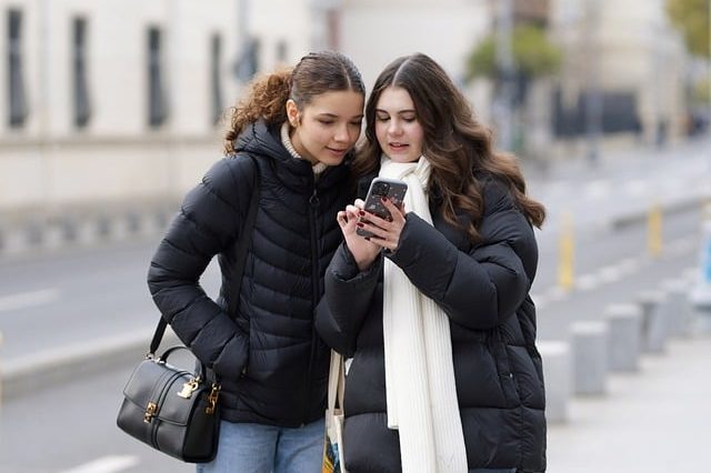 Deux jeunes femmes en vestes d'hiver regardant ensemble un iPhone haut de gamme dans une rue de la ville.