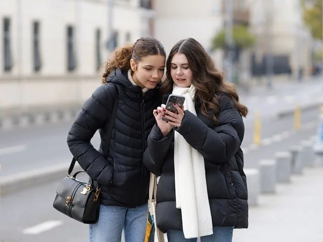 Deux jeunes femmes en vestes d'hiver regardant ensemble un iPhone haut de gamme dans une rue de la ville.