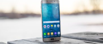 Un smartphone avec un écran clair posé debout sur une surface en bois avec un fond flou d'eau et de ciel, symbolisant l'évolution des smartphones.