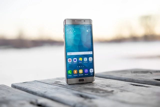 Un smartphone avec un écran clair posé debout sur une surface en bois avec un fond flou d'eau et de ciel, symbolisant l'évolution des smartphones.