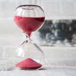 Un sablier avec du sable rose sur un journal, capturant l'écoulement du temps sur un fond flou d'article de presse sur la gestion du temps.