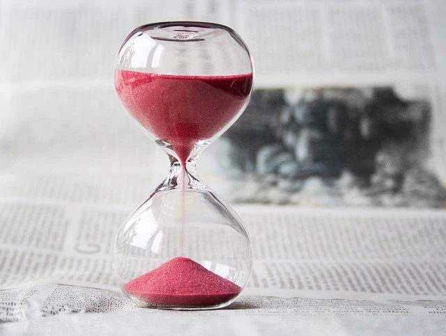 Un sablier avec du sable rose sur un journal, capturant l'écoulement du temps sur un fond flou d'article de presse sur la gestion du temps.