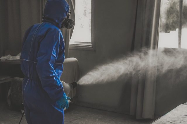 Personne portant un équipement de protection bleu utilisant une machine à brouillard à l'intérieur.