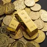 Des lingots d'or et diverses pièces d'or sont élégamment exposés sur une surface sombre, invitant subtilement à la contemplation des facteurs influençant le prix de l'or.