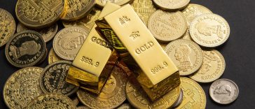 Des lingots d'or et diverses pièces d'or sont élégamment exposés sur une surface sombre, invitant subtilement à la contemplation des facteurs influençant le prix de l'or.