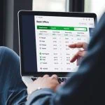 Une personne utilise un ordinateur portable pour consulter un tableau comparatif des offres des banques en ligne, y compris les taux d'intérêt comparatifs 2025 et les offres de remise en argent, dans une application de gestion financière.