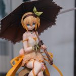 Une figurine geek chic d'une fille de style anime aux cheveux blonds courts, portant une robe crème et tenant un parasol noir, est assise sur le présentoir - un parfait objet de collection pour tout fan.
